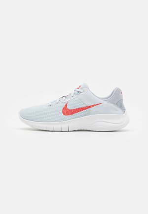 Lichtgrijze sportschoen met rode Nike-swoosh, witte flexibele zool en ademend mesh bovenwerk, zijaanzicht op witte achtergrond.