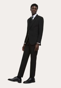 Czarny garnitur z dopasowaną marynarką i spodniami, ozdobiony zamknięciem na trzy guziki i bocznymi kieszeniami, w połączeniu z białą koszulą i krawatem.