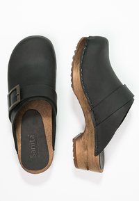 Sorte læderklipklappere med spænde, træhæl og syede detaljer. Rund tå-design og åben bagfor for nem påklædning.