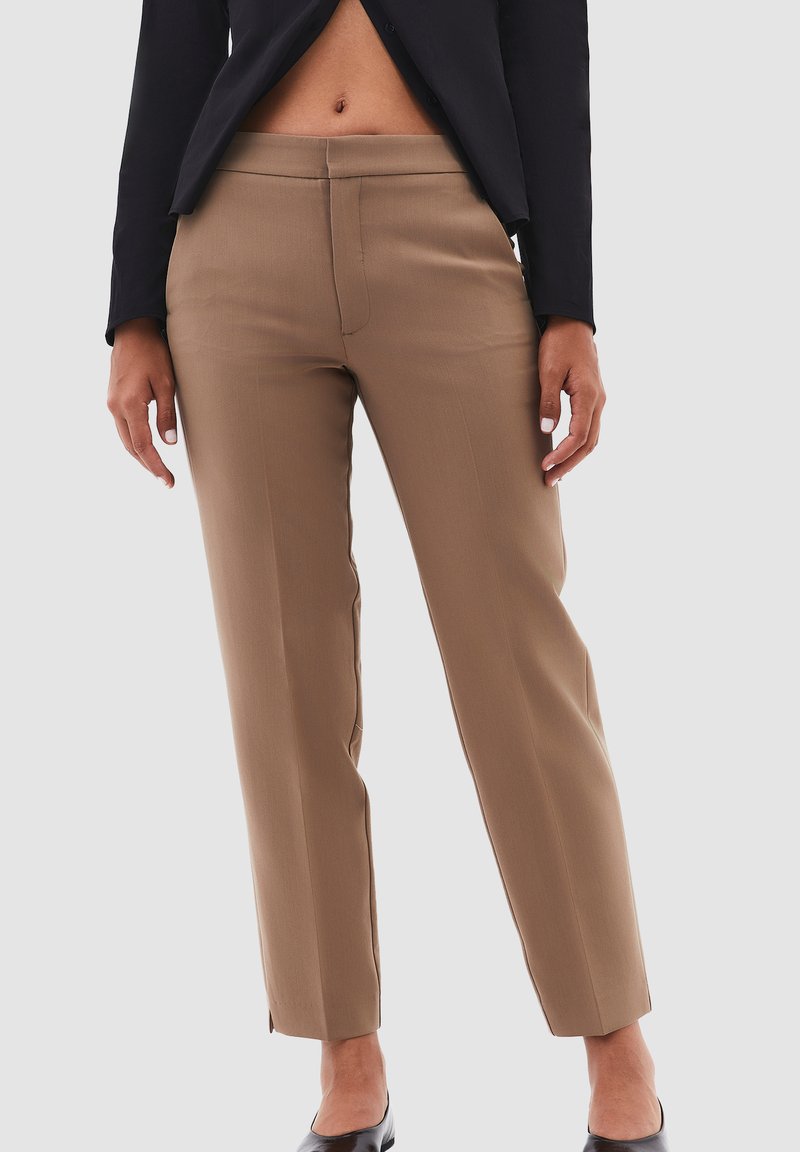 Bruine op maat gemaakte broeken met een rechte pijp, gekenmerkt door een gladde textuur en een naad aan de voorkant. Gestyled met een zwarte blazer.
