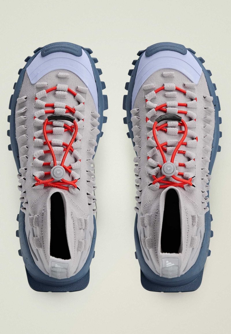 Scarpe da ginnastica grigie chiare con lacci rossi, tomaia texturizzata, suola blu e accenti a motivo. Presenta una linguetta e un sistema di lacci unico.