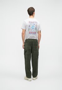 Ανοιχτό γκρι μπλουζάκι με πολύχρωμο γεωμετρικό σχέδιο χεριού και μοτίβα της φύσης. Ελαιόχρωμο παντελόνι cargo από κορδούρα με πολλές τσέπες.