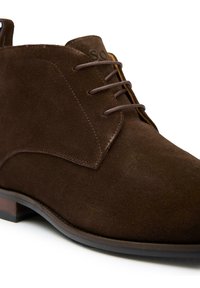 Brown suede ankle boots with a smooth texture, featuring a lace-up design, subtle stitching, and a brown sole. Branding visible near the top.