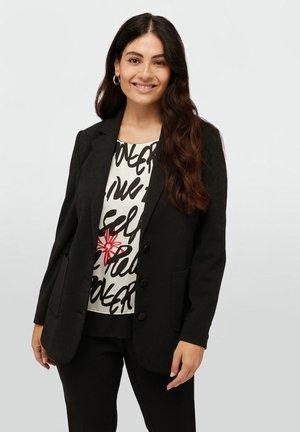 Blazer noir à deux boutons, avec un col cranté et des poches. Haut blanc en dessous avec du texte noir et un accent floral rouge.