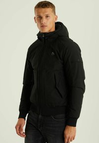 Crna zip-up kapuza jakna s teksturiranim završetkom, koja ima dva bočna zip džepa i detalj loga na prsima. Rebrasti rukavi i donji rub.