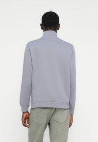 Jasnoszara bluza z wysokim kołnierzem, ściągaczami na rękawach i prostym dołem. Wykonana z miękkiego materiału, prezentująca czysty wzór bez wzorów.