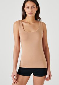 Top senza maniche beige realizzato in tessuto morbido, caratterizzato da un collo a giro e una vestibilità slim, abbinato a pantaloni corti neri.