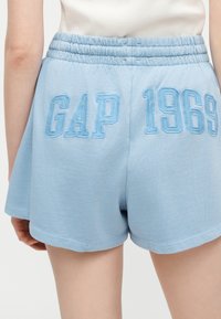 Shorts bleu clair à taille élastique avec "GAP 1969" brodé au dos, portés par une personne en haut blanc.