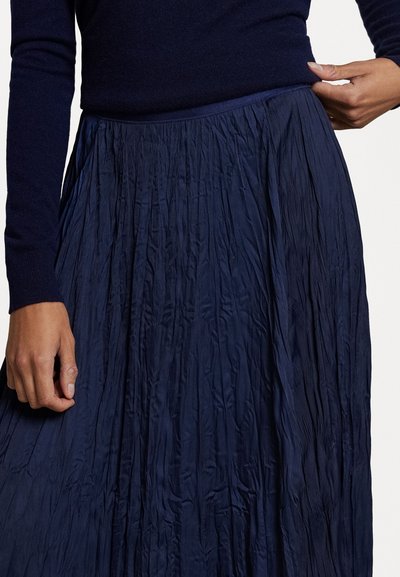 Námornícky, textúrovaná plisovaná sukňa so priliehavým pásom. Tkanina sa elegantne splýva, ukazuje jemný lesk a zložitú plisovanú štruktúru.