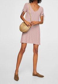 Pasiasta sukienka z krótkimi rękawami i dekoltem w kształcie V. Paski są czerwone na jasnym tle. Połączona z plecioną torbą i brązowymi płaskimi butami.