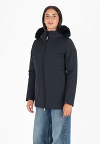 Zwarte geïsoleerde jas met een met bont gevoerde capuchon, voorzien van een volle frontrits, zijzakken en lange mouwen. Glad, waterafstotend materiaal.