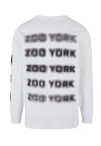 White long-sleeve shirt featuring repeated black spray-painted "ZOO YORK" text in varying opacity across the back. Cotton material.