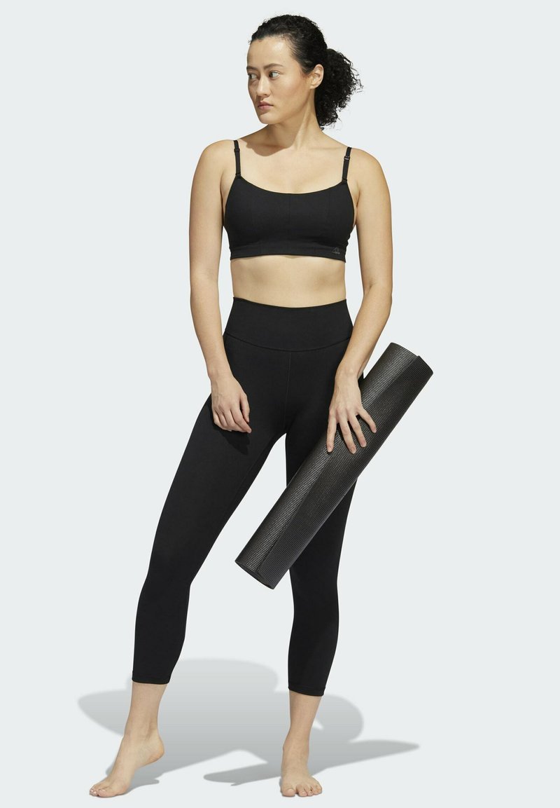 Haut de sport noir court et leggings taille haute, accompagnés d'un tapis de yoga noir texturé, présentant un design lisse et ajusté.