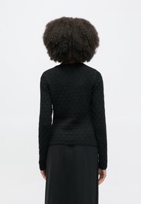 Čierny textúrovaný top s dlhým rukávom a okrúhlym výstrihom, priliehavý strih a jednoduchý dizajn, v kombinácii s dlhou čiernou sukňou.