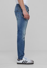 Világoskék farmernadrág, slim fit fazonban, szakított részletekkel, hátsó zsebekkel és a derékpánthoz rögzített ezüst lánccal.