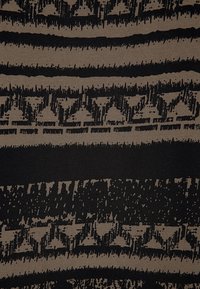 Textil med djärva svarta mönster på en beige bakgrund, med horisontella ränder och varierande texturer. Mönstren inkluderar taggiga linjer och prickar.