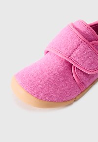 Pink felt shoe with a rounded toe, velcro strap, and tan rubber sole. Soft texture with stitching details and a seamless design.
