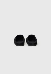 Black slide sandals with a soft, textured fabric upper, open toe design, and thick, flat rubber sole. Minimalist and simple styling.
