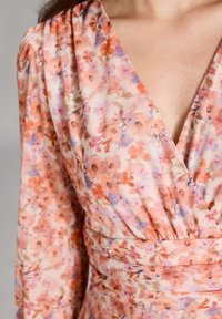 Kukkaprintilla varustettu kietaisumekko pehmeässä, kevyessä kankaassa. Ominaisuuksiin kuuluu persikan ja violetin kukkien sävyjä, syvä V-kaula-aukko ja kootut yksityiskohdat vyötäröllä.