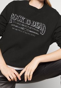 Felpa nera con stampa argentata che riporta il testo "IL ROCK È MORTO, È TUTTO RIGUARDO L'ATTEGGIAMENTO. NESSUN RAGAZZO, NESSUN FUTURO." Collo e polsini a costine.