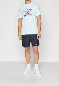 Světle modré bavlněné tričko s vícemenším logem Nike, doplněné černými sportovními šortkami a bílými teniskami.