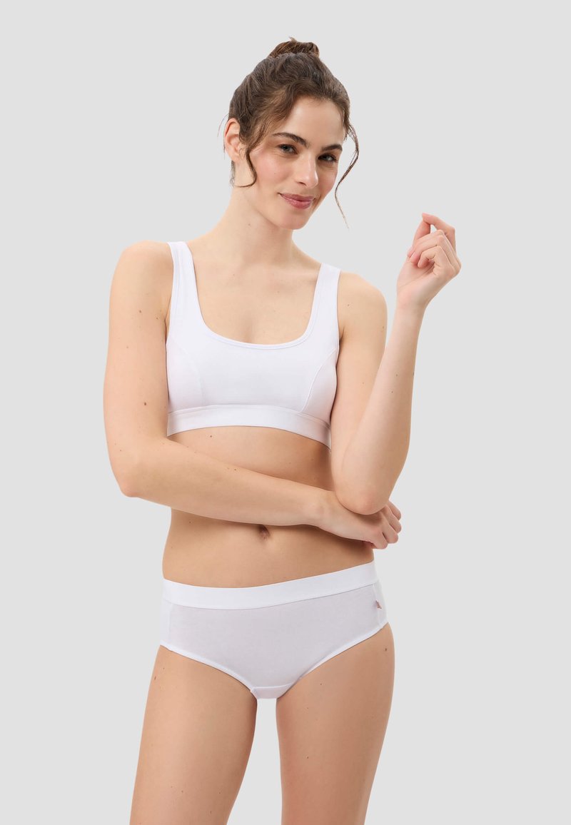 Weißer Sport-BH mit quadratischem Ausschnitt und breiten Trägern, kombiniert mit weißen Hipster-Slips, die einen weichen Bund und ein Logo-Detail aufweisen.