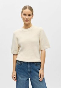 Pull beige à manches courtes en tricot avec un col rond côtelé. Assorti à un jean en denim bleu taille haute. Texture de tissu lisse.