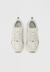 Světle šedé běžecké boty s průhlednými panely, pastelově růžovými akcenty a reflexními detaily. Mají ploché tkaničky a polstrované límce.