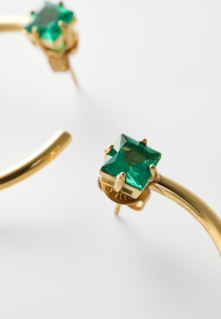 Pendientes de aro dorados con gemas verdes de corte cuadrado engastadas en garras sobre un fondo blanco limpio.