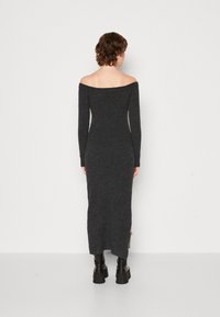 Langärmeliges, tailliertes, schulterfreies Kleid aus dunkelgrauem Strick mit langen Ärmeln und seitlichem Schlitz. Stilisiert mit klobigen schwarzen Stiefeln.