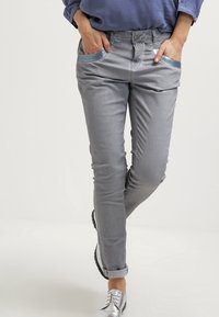 Šedé kalhoty se slim fit střihem, zdobené texturovanými modrými akcenty na kapsách. Vyrobené z hladkého materiálu, spojují pohodlí s ležérním designem.