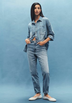 Cămașă din denim de culoare albastru deschis, cu o croială supradimensionată, închidere cu butoane și accente subtile. Blugi asortați de culoare albastru deschis, cu detalii cu ținte. Pantofi albaștri slip-on.