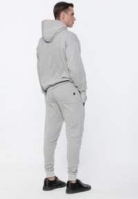 Szary hoodie i pasujące dresy wykonane z miękkiego, teksturowanego materiału. Hoodie ma szew z tyłu i kieszeń kangurzą; spodnie mają elastyczne mankiety.