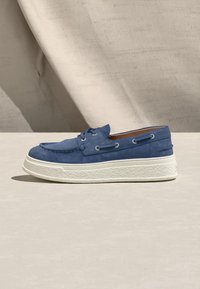 Μπλε καστόρινο παπούτσι σκάφους με λευκή υφή στη σόλα πλατφόρμας, λεπτομέρειες με κορδόνια και μοκ το, φωτογραφημένο σε μπεζ επιφάνεια και φόντο.