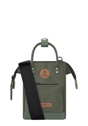 Small vertical olive-green leather handbag with black adjustable shoulder strap and front zip pocket, featuring Cabaia logo patches.