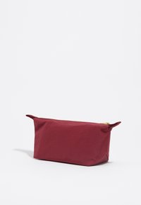 Neceser rectangular burdeos con una cremallera dorada, fabricado en material texturizado. Cuenta con dos pequeñas asas de tela en cada extremo.