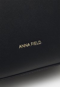Czarna torebka z fakturowanej skóry z złotym logo "ANNA FIELD". Powierzchnia ma delikatny wzór, co zwiększa jej elegancki wygląd.