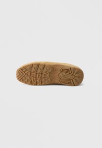 Tan rubber shoe sole with textured tread pattern, featuring deep grooves and multi-directional lugs for traction and grip.