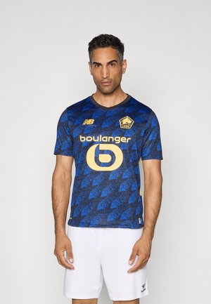 Blauwe voetbalsjerp met driehoekige patronen, voorzien van een gele logo en tekst. Korte mouwen en een ronde halslijn, gecombineerd met witte shorts.