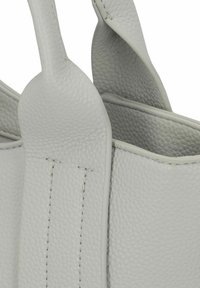Sac à main en cuir gris clair avec une surface texturée, dotée de poignées arrondies et de coutures visibles le long des bords. Aucune ornementation présente.