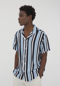 Camicetta a maniche corte con bottoni, caratterizzata da righe verticali in blu, nero e bianco. Realizzata in un tessuto leggero con una vestibilità comoda.