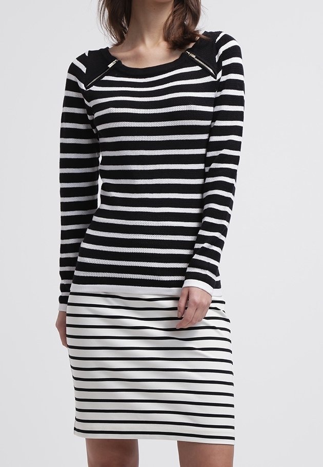 Schwarz-weiß gestreiftes Langarmoberteil mit rundem Ausschnitt, kombiniert mit einem engen schwarz-weiß gestreiften Rock. Auffällige Reißverschlüsse an den Schultern.