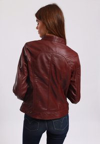 Burgundy leather jacket with a fitted design, high collar, and tailored seams, paired with dark denim jeans. Smooth texture, minimal hardware.
