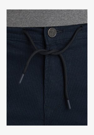 Pantalones de pana en color navy con un cordón negro y un botón metálico redondo. La textura es acanalada y hay un detalle de costura visible.