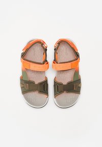 Sandaali, jossa on vaaleanharmaa kumipohja, oliivinvihreät nylon-nauhat ja kirkkaan oranssit yksityiskohdat. Säädettävät soljet varmistavat mukautuvan istuvuuden.