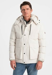Giubbotto puffoso bianco con cappuccio, dotato di zip e chiusura a pressione, ampie tasche frontali e lacci neri per la regolazione.