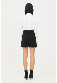 Camicia bianca a maniche lunghe con colletto abbinata a pantaloni corti neri a vita alta. Il modello indossa anche stivaletti neri con tacco.
