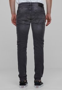 Hallid slim-fit teksad, millel on kulunud tekstuur ja kaks tagataskut. Kandmisel mustad tenniseketsid valgete aktsentidega.
