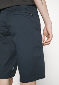 Shorts bleu foncé en tissu durable, dotés de deux poches latérales et d'un logo de marque visible sur la taille.