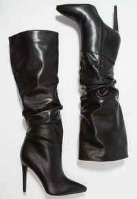 Botas negras de cuero hasta la rodilla con un diseño holgado, punteras afiladas y tacones de aguja altos. Presenta un detalle de cremallera en el costado para el cierre.